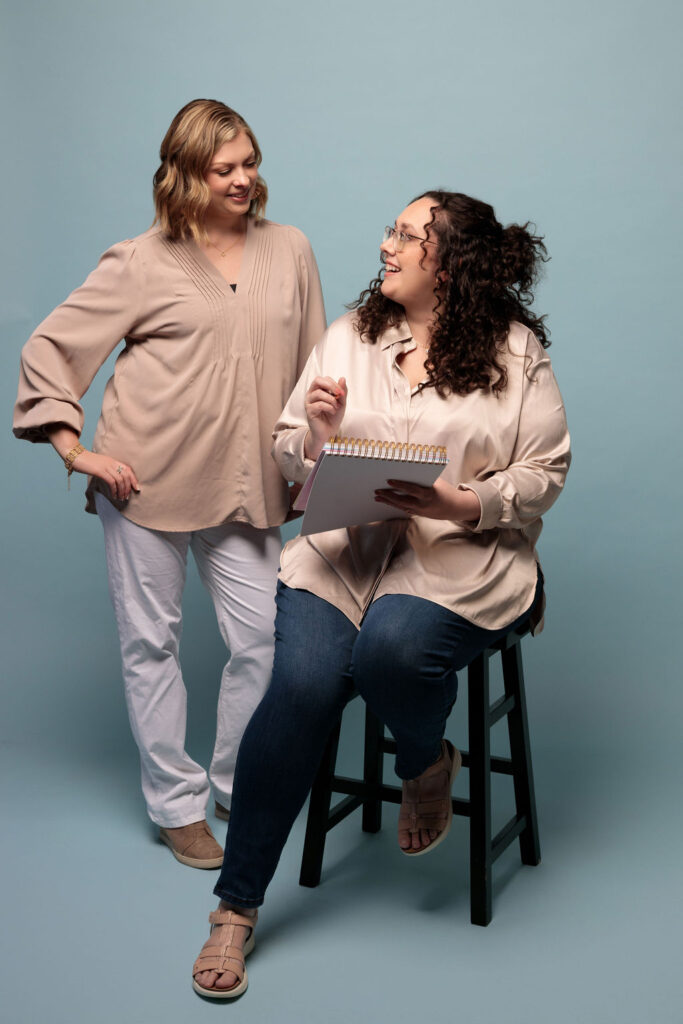 Founder's Nicole and Maureen of Revonish Content Lab looking at each other for inspiration.  Nicole on stool, Maureen standing